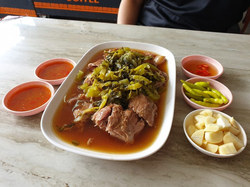 ขาหมูพะโล้จานใหญ่ในน้ำพะโล้ โปะผักกาดดอง วางคู่ถ้วยน้ำจิ้ม พริก และกระเทียม
