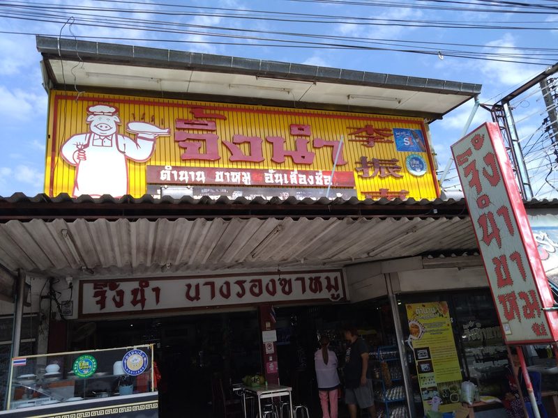 หน้าร้านจิ้งนำ ป้ายเหลืองรูปพ่อครัวหมูถือจาน และป้ายแดง จิ้งนำ นางรองขาหมู เหนือหน้าร้าน