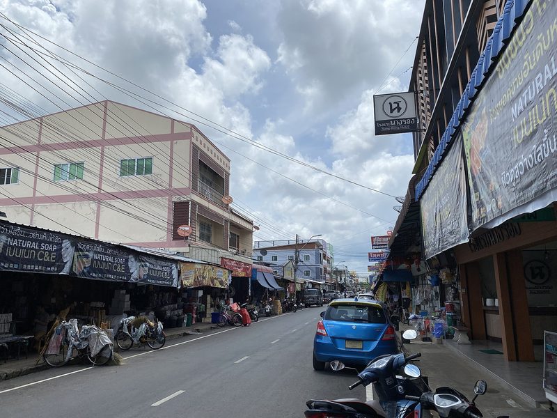 ถนนในตัวเมืองนางรอง ห้องแถวสองฝั่ง มีรถจอดริมทางใต้ฟ้าโปร่ง